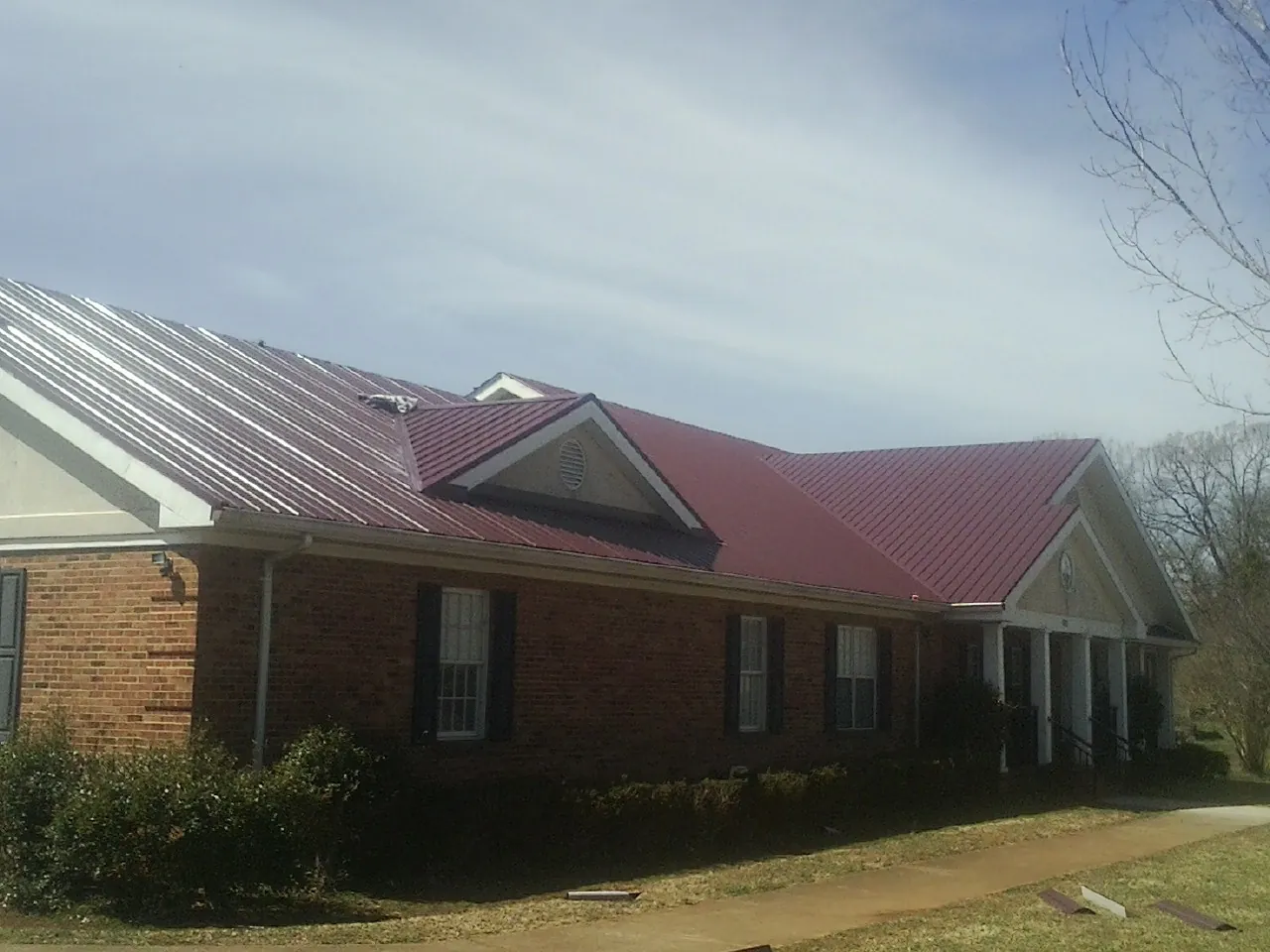 Red metal roof with gabled entries on a long brick building, from a Hail Damage Roof Repair job in Lake City